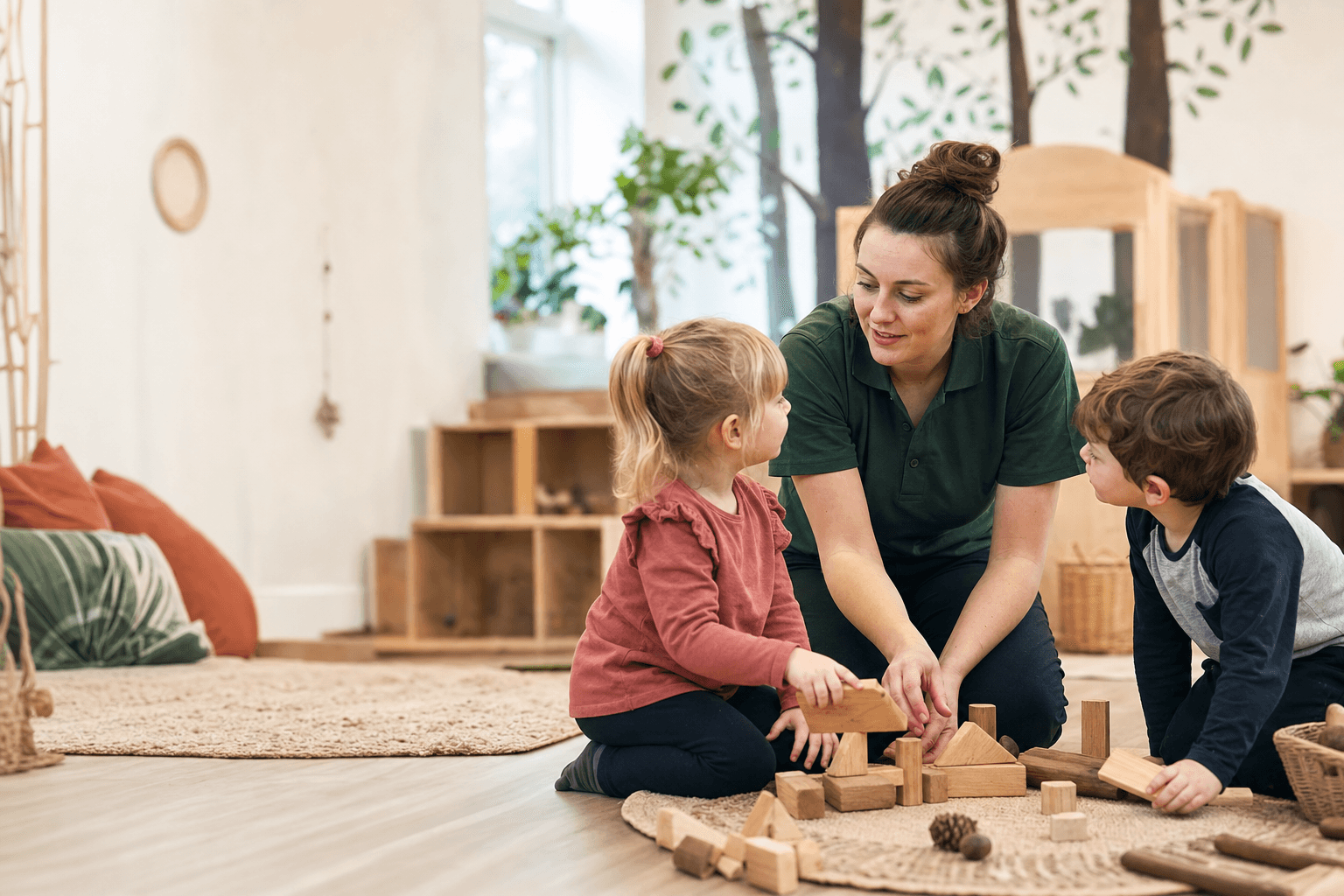 A practitioner helping two children take turns while playing with wooden blocks